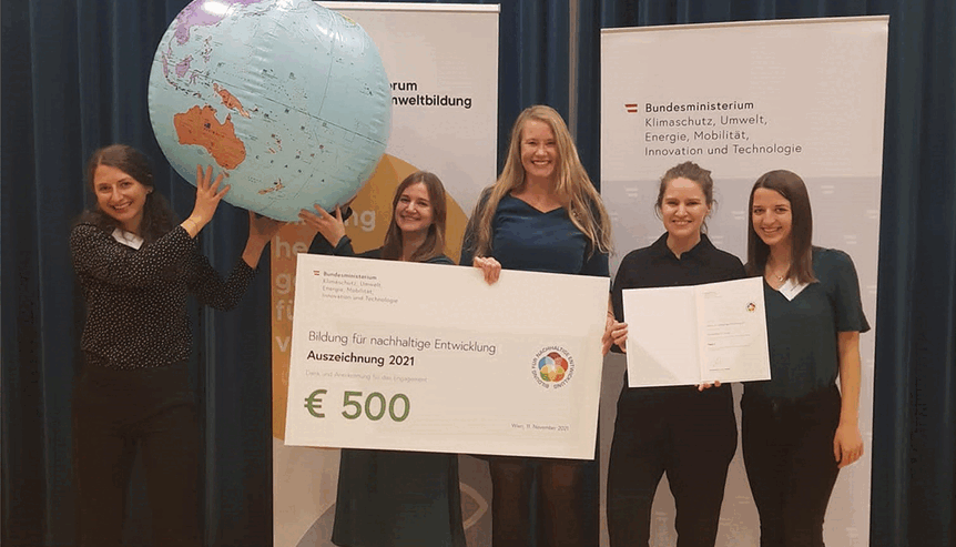 FIve people holding a large cheque over 500€ and an inflatble globe